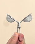 Metallic butterfly-shaped strainer held by a hand against a beige background