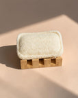 Zero Waste Outlet natural bamboo soap dish with angled slats and non-slip silicone pads, holding a white loofah sponge.