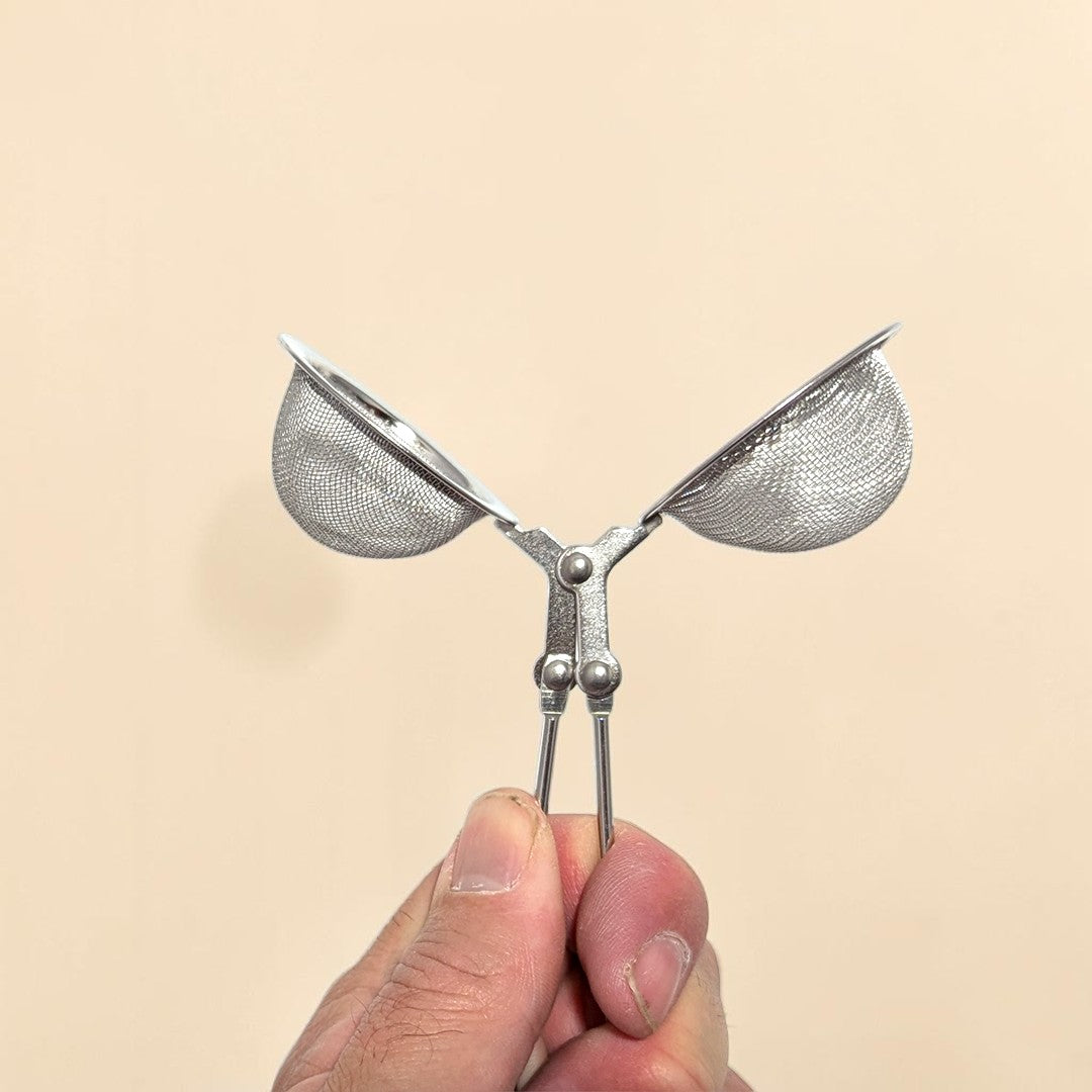 Metallic butterfly-shaped strainer held by a hand against a beige background