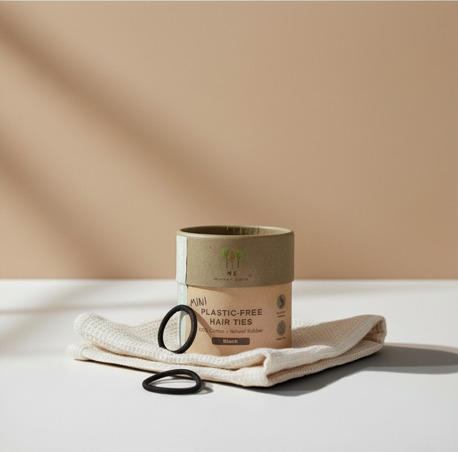 Zero Waste Outlet mini black organic cotton hair ties in a plastic-free cardboard tube on a white cloth surface